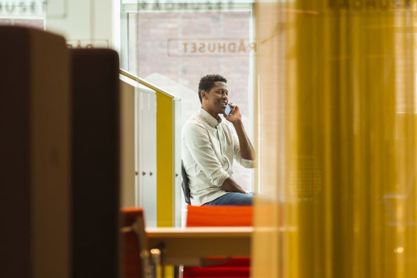 Man talking on the phone while using hot desk in a modern office environment. 