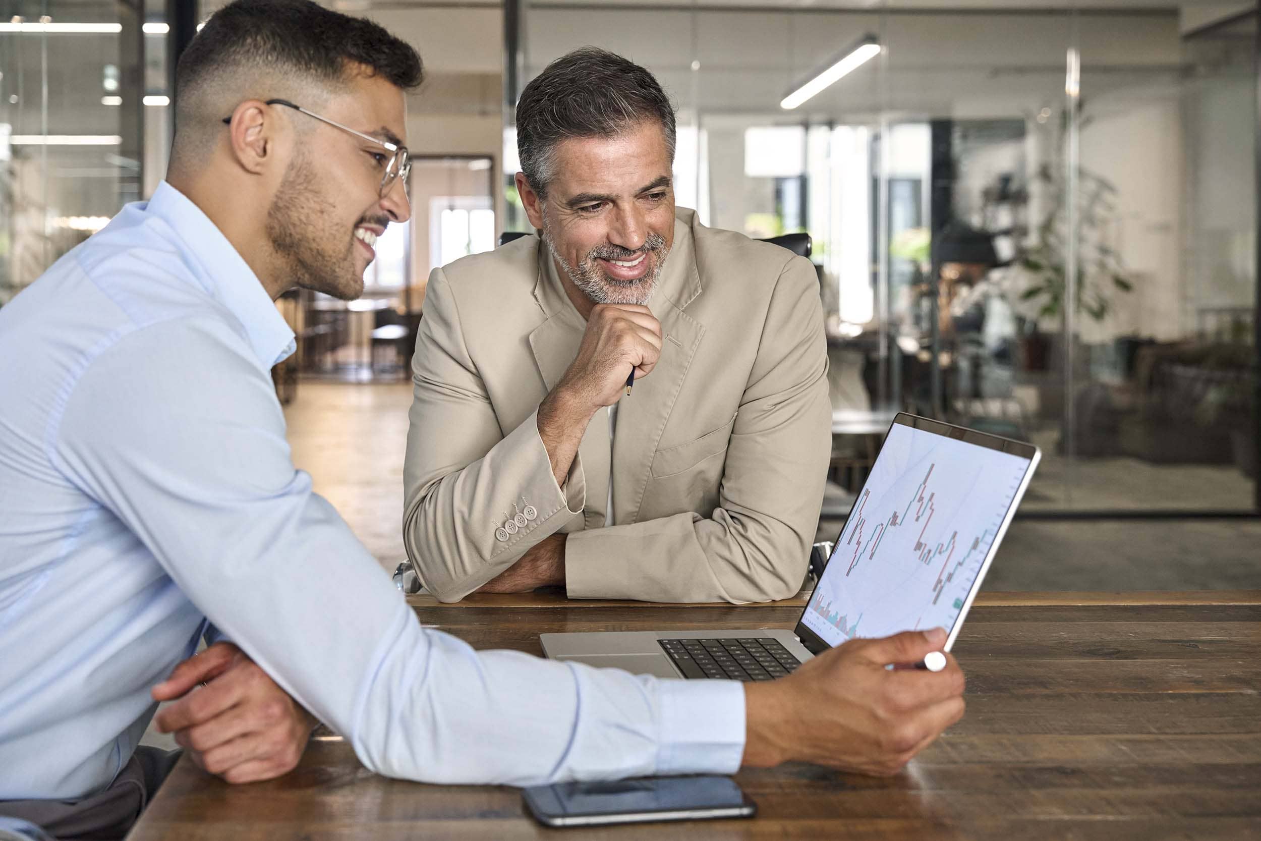 Two professionals reviewing data on a laptop in a glass-walled meeting room, reflecting digital collaboration and strategic planning in a hybrid workplace environment.