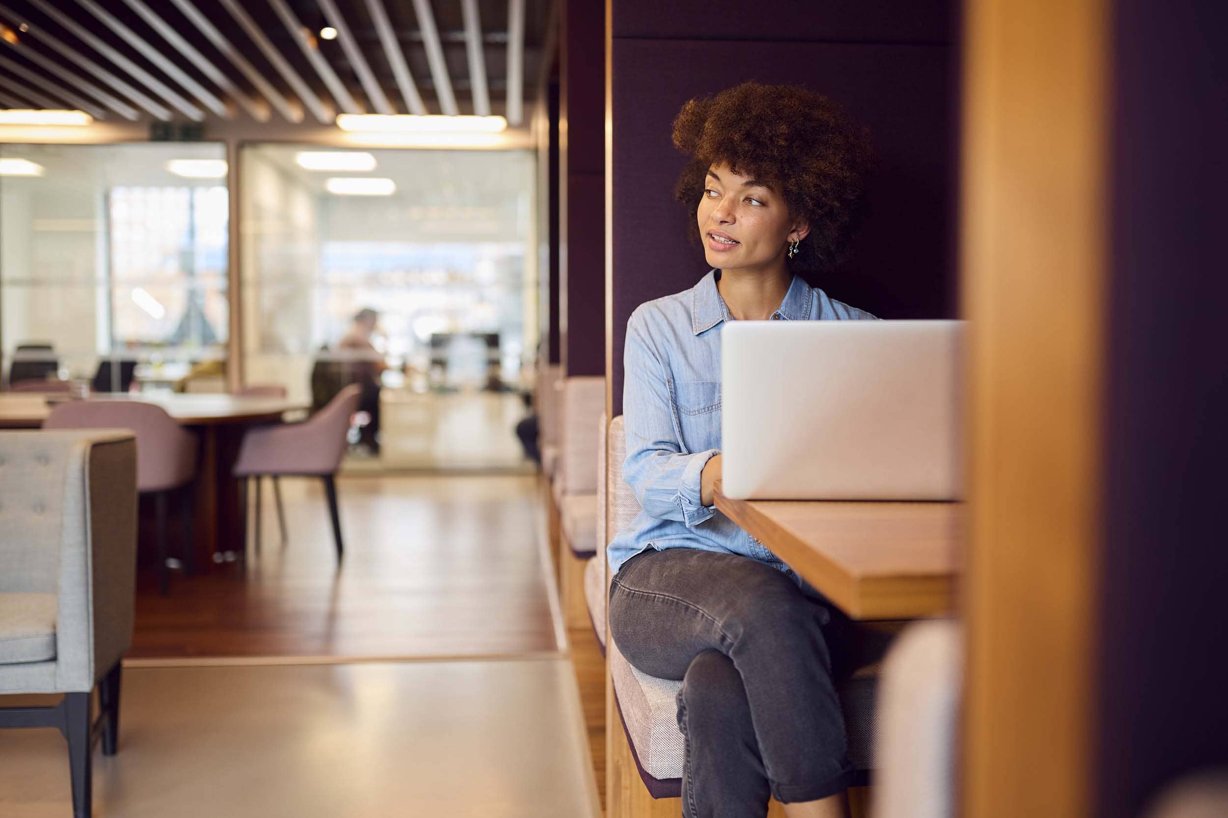 Woman working on a laptop in a quiet booth within a modern hybrid office, representing flexible workspace design that supports focus and individual productivity.