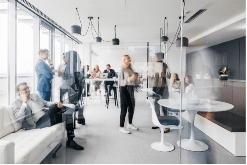 Colleagues meeting and working in a bright open-plan office with lounge seating, high tables and a glass-walled meeting area.