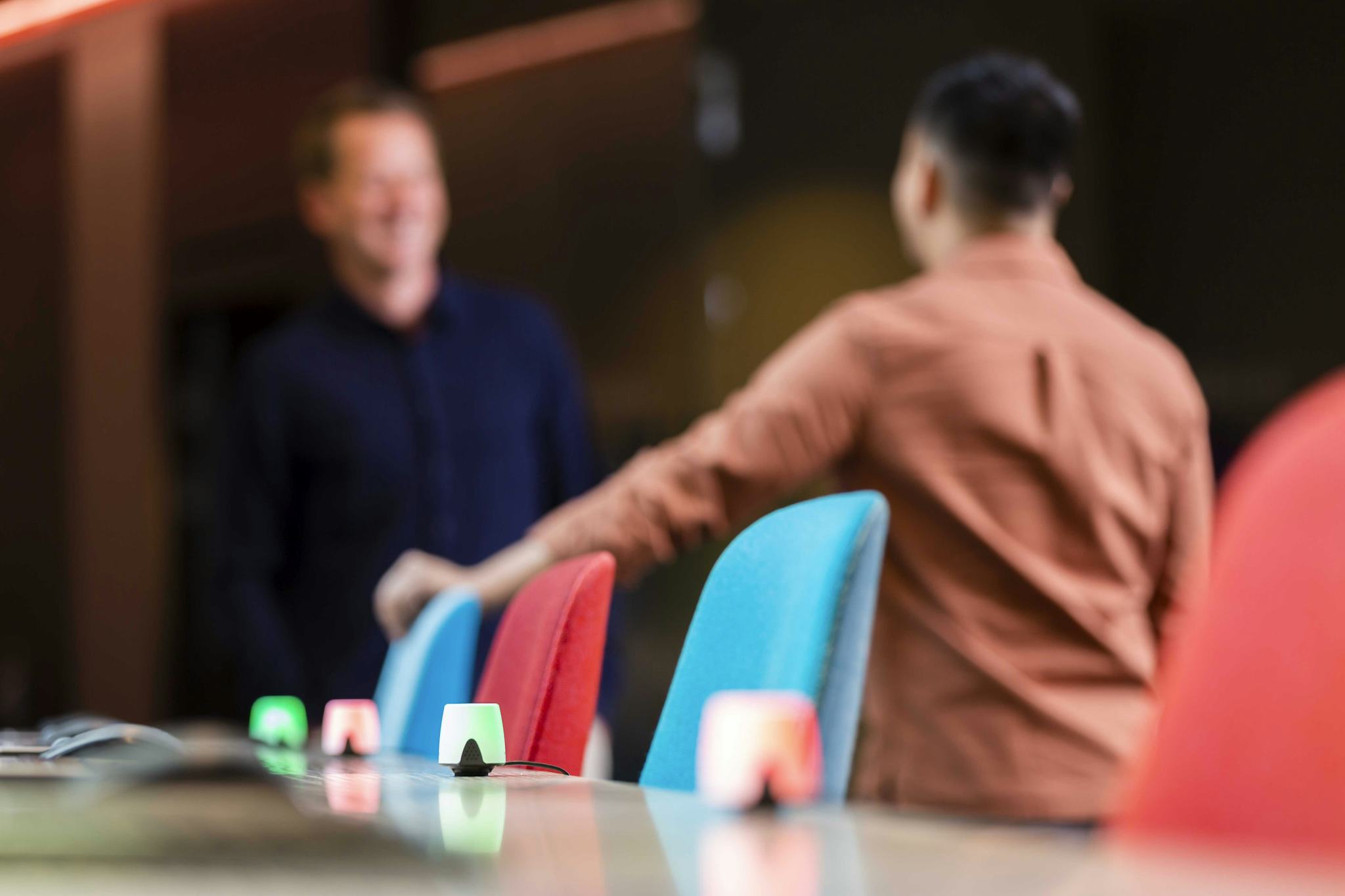 People chatting in the background in front of desks where busy lughts are displayed, showing the desks availability through color indication. 