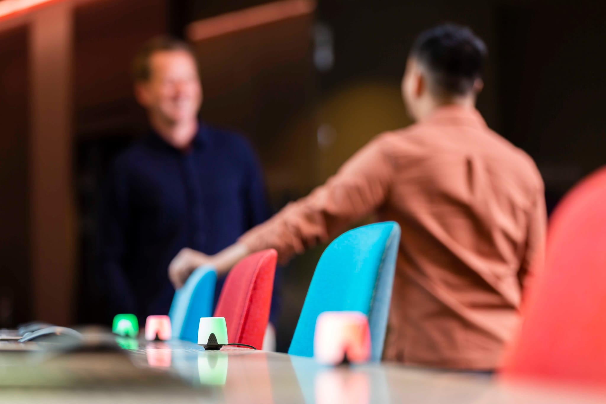 People chatting in the background in front of desks where busy lughts are displayed, showing the desks availability through color indication.