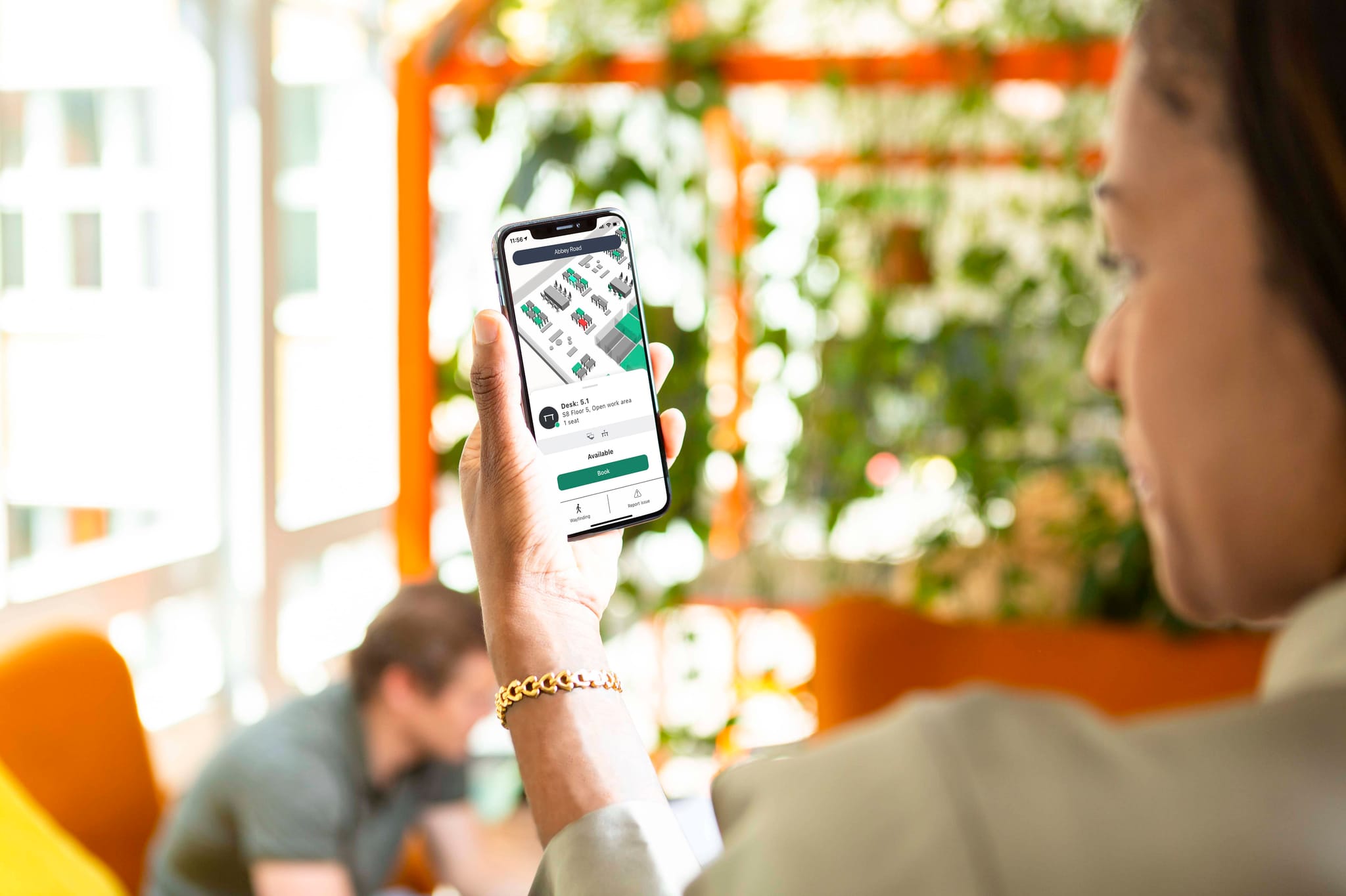 woman holding up her phone and making a dek booking from flowscape's smartphone app, man sitting in a chair blurred in the background.